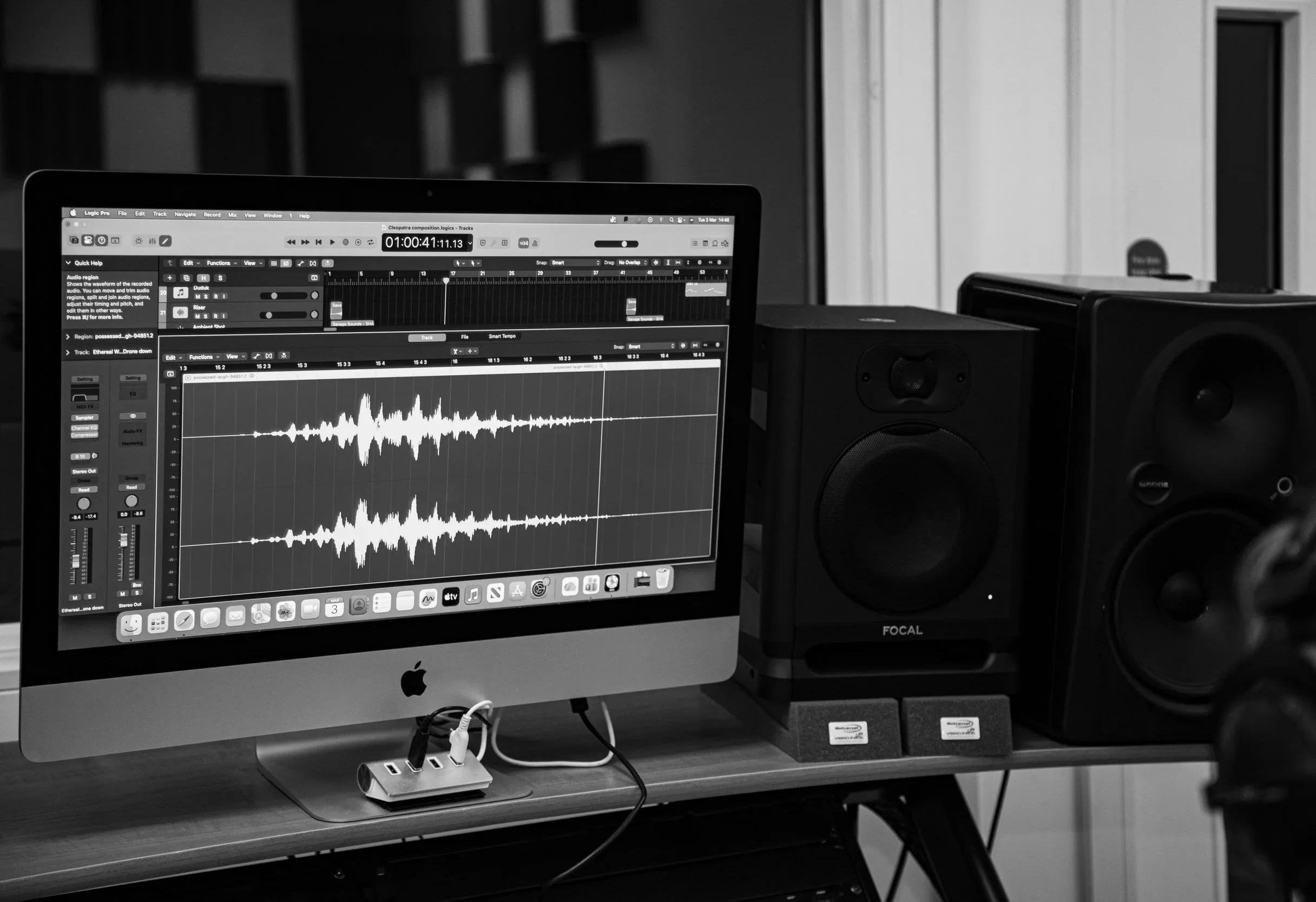 A computer monitor displaying audio editing software with sound waveforms, stacked on a desk alongside studio speakers.