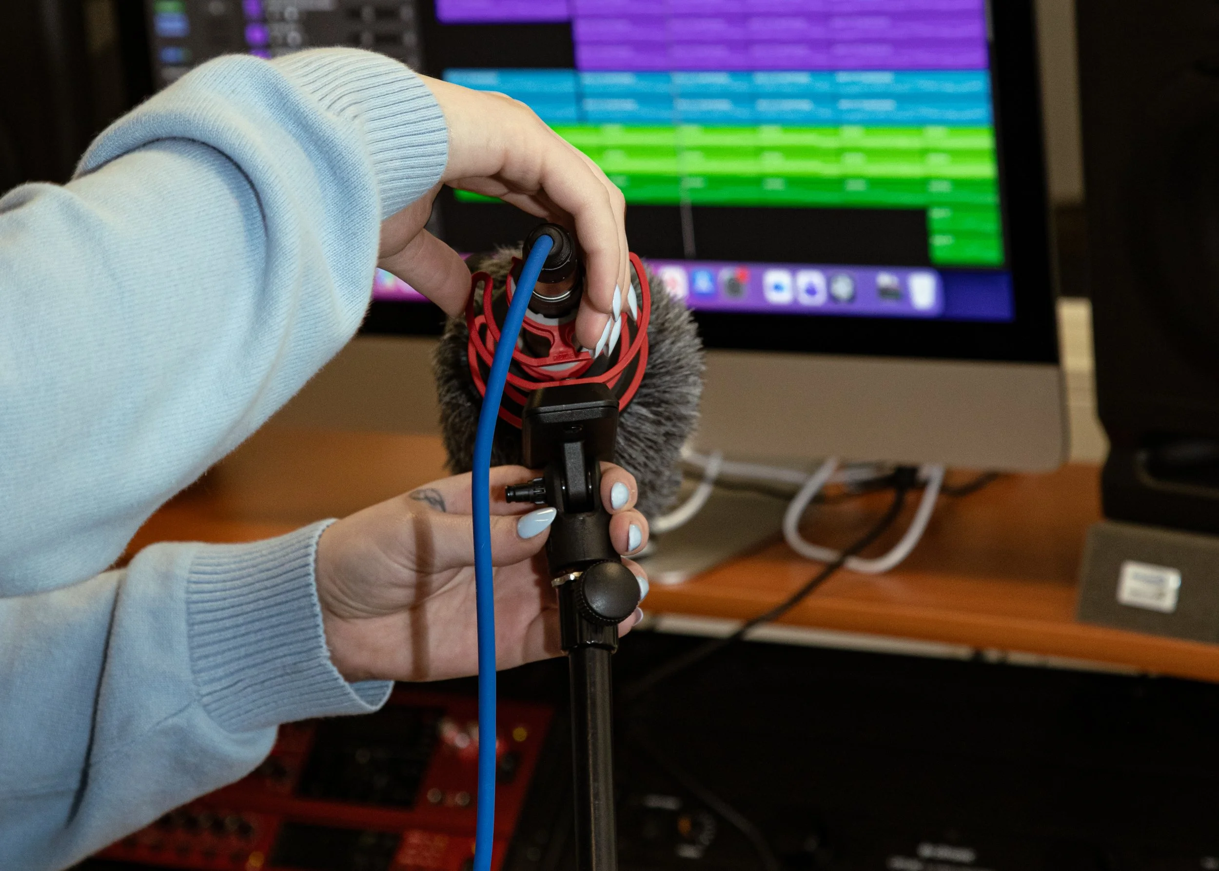 Person adjusting audio equipment in front of a computer screen with colorful waveforms.