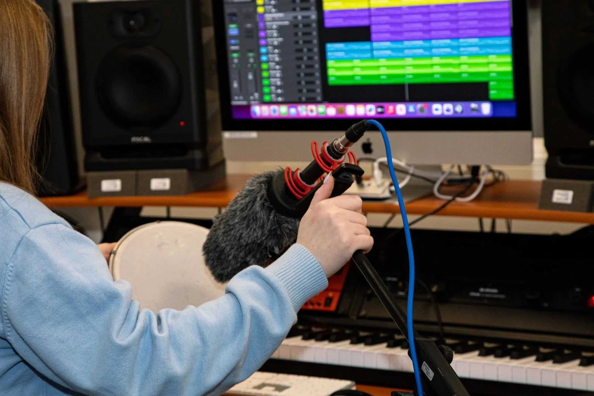 Person holding a microphone near a computer monitor displaying audio editing software