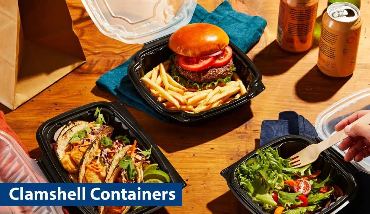 Assorted takeout food containers on a wooden table, including a burger with fries, tacos, and a salad, with cans of soda and a paper bag nearby.