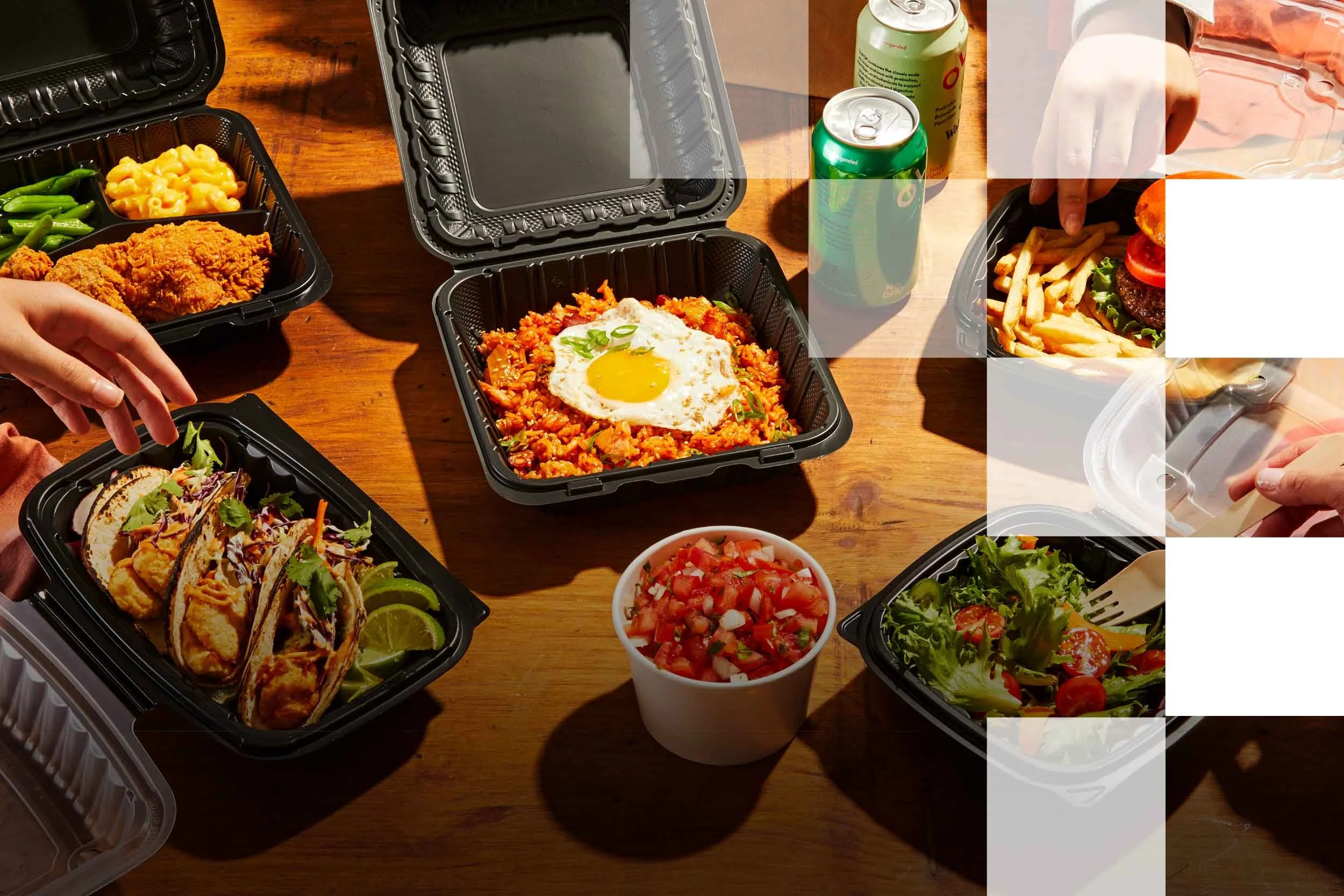 Food containers with tacos, fried chicken, pasta, salad, and beverages on a wooden table.
