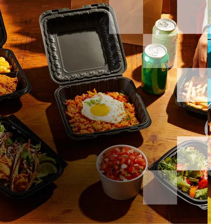Food containers with tacos, fried chicken, pasta, salad, and beverages on a wooden table.