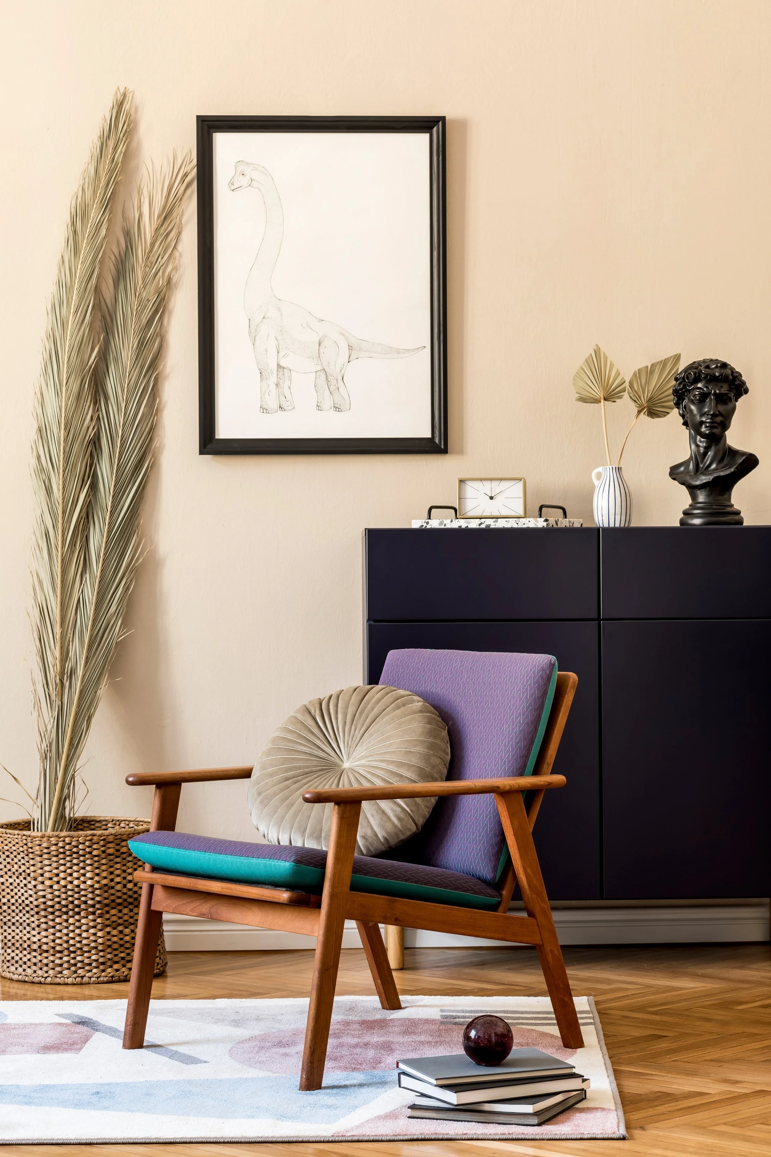 Living room corner with a purple and teal mid-century modern chair, decorative pillows, a black cabinet with art and decor items, and a framed elephant sketch on the wall.