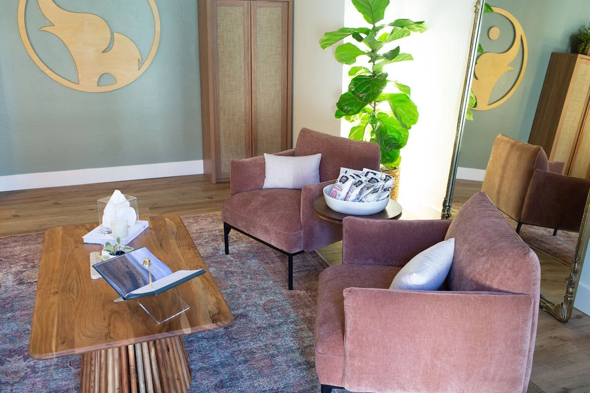 A cozy waiting room with two pink upholstered armchairs positioned around a wooden coffee table. 