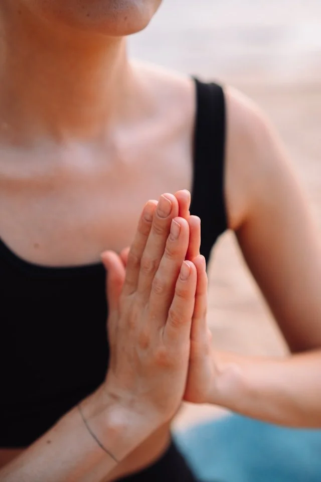 A person in a black tank top with their hands in a prayer position.