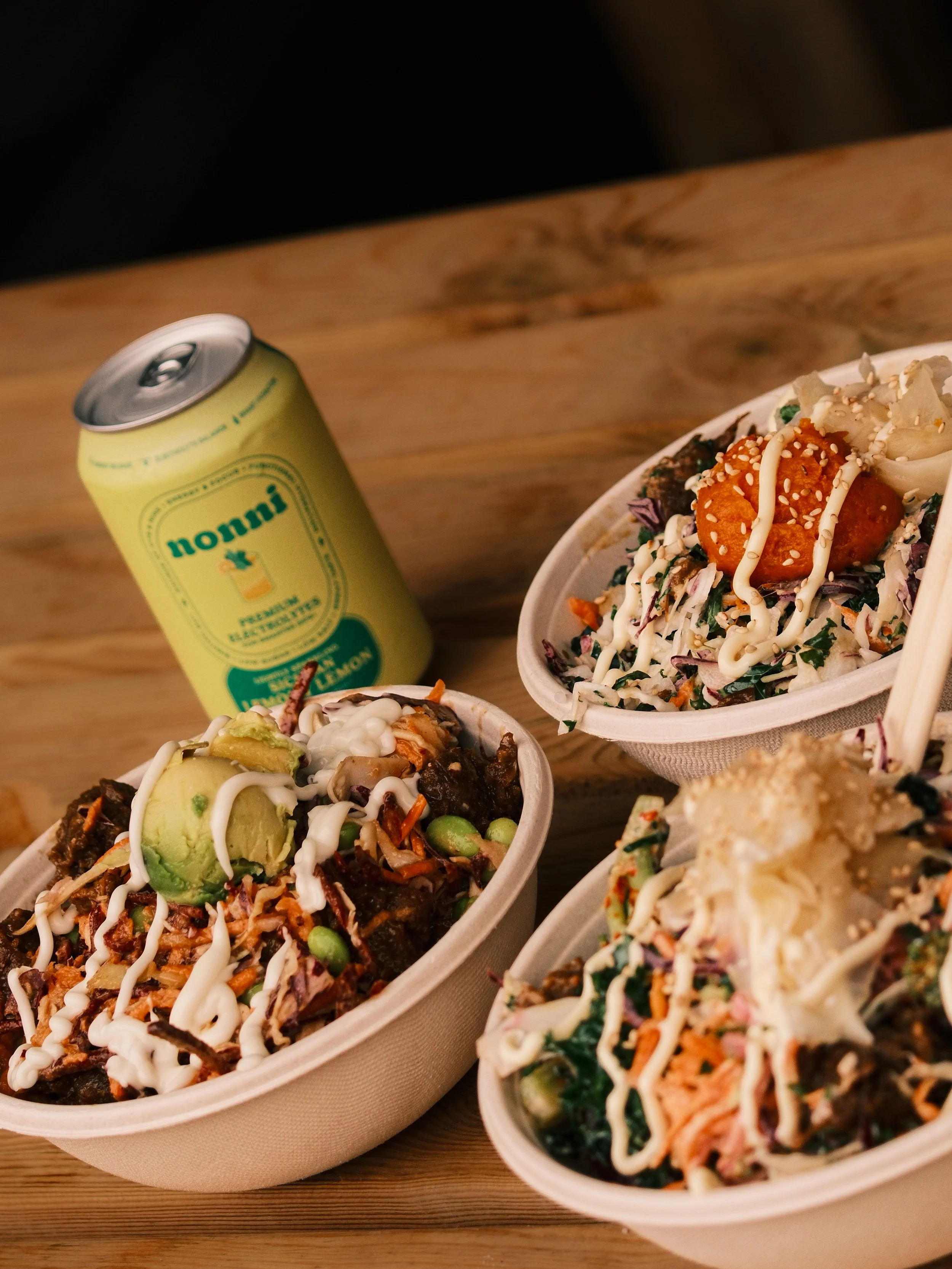 Assorted sushi bowls topped with sauces and garnishes on a wooden table.