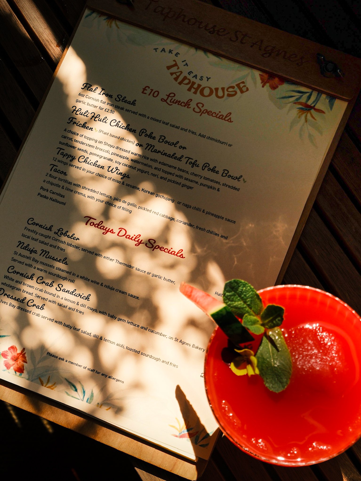 A menu for Take It Easy Tap House displaying lunch specials and a bright red cocktail with mint leaves and a slice of watermelon in the foreground.