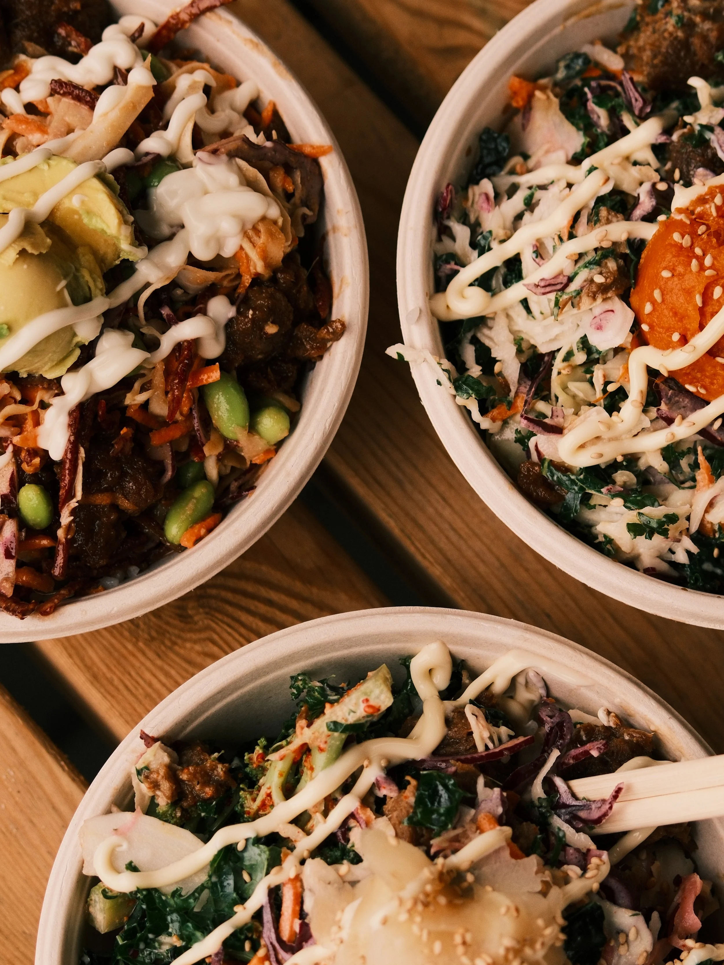 Three bowls of salad with various vegetables, drizzled with creamy dressing, and topped with sesame seeds and chopped herbs.