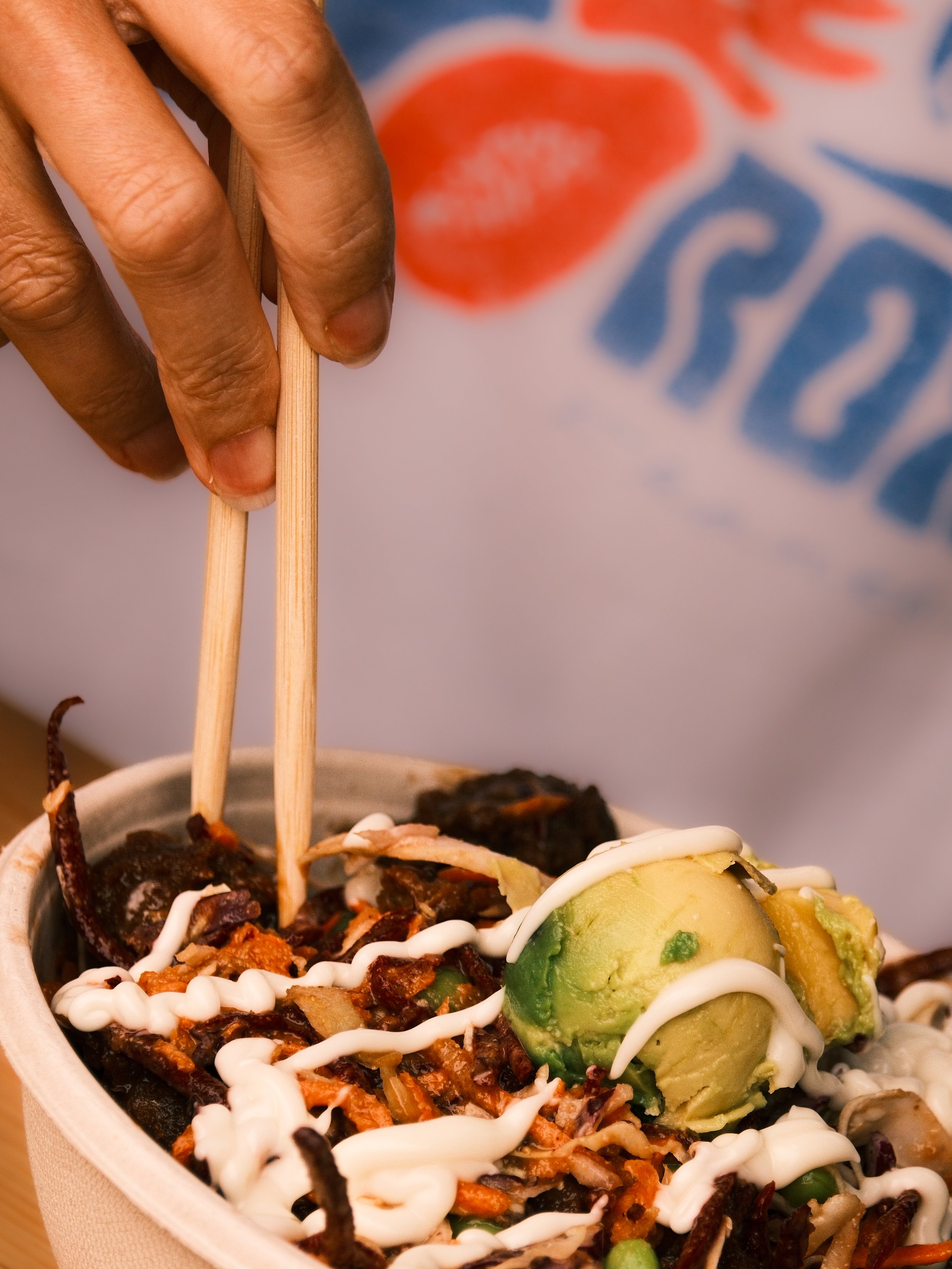 Close-up of a bowl of Mexican street corn with jalapenos, herbs, and mayonnaise, and a hand holding chopsticks.