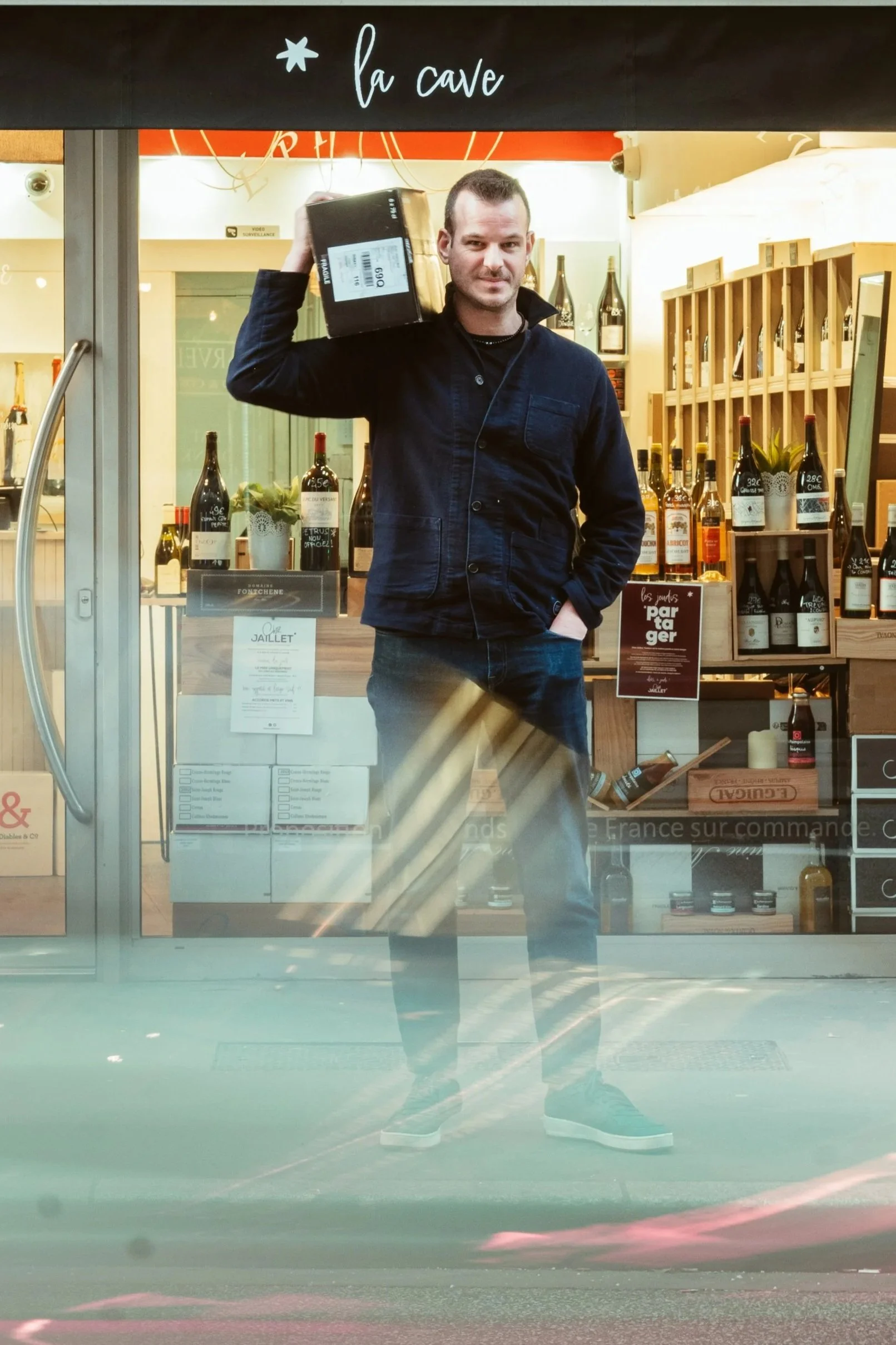 Chez Jaillet Lyon 6 | Alexis, le caviste Chez Jaillet, se tient devant la Cave avec une sélection de vins.