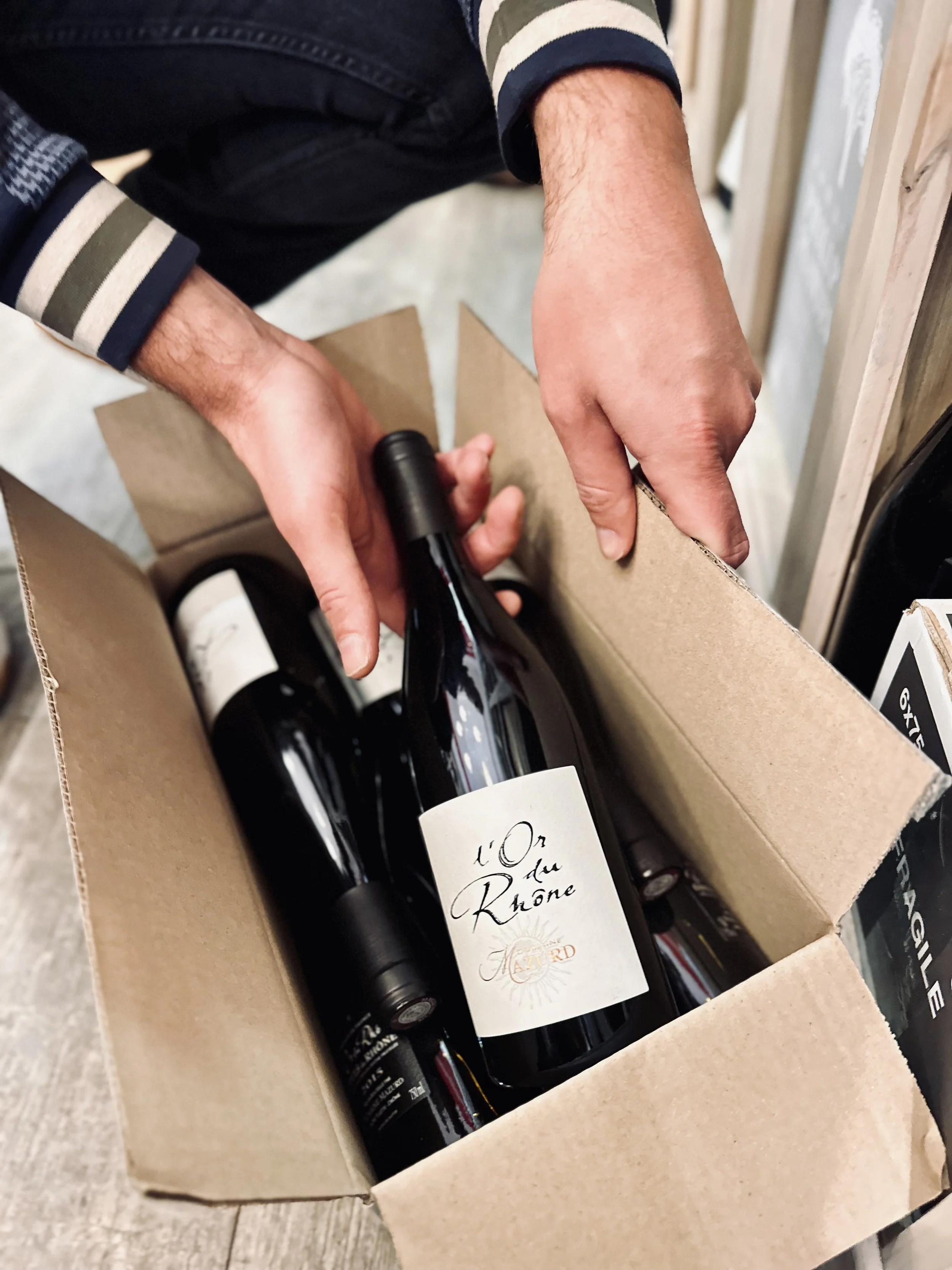 Chez Jaillet Lyon 6 | Alexis, le caviste de Chez Jaillet, tient une bouteille de vin dans une caisse en carton à la Cave Lyon 6.