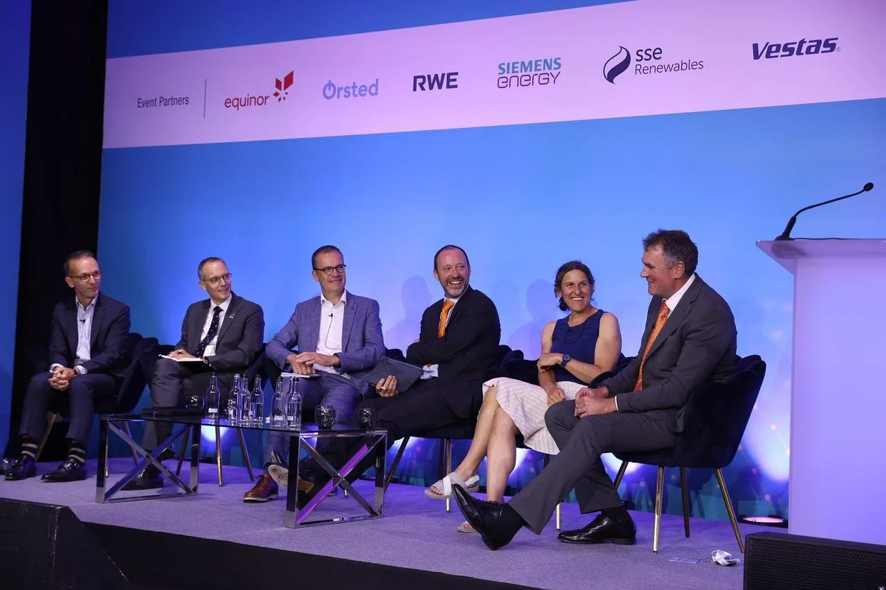 Six people sitting on stage at a panel discussion, with a blue background displaying logos of various companies, including equinor, Orsted, RWE, Siemens Energy, SSE Renewables, and Vestas.