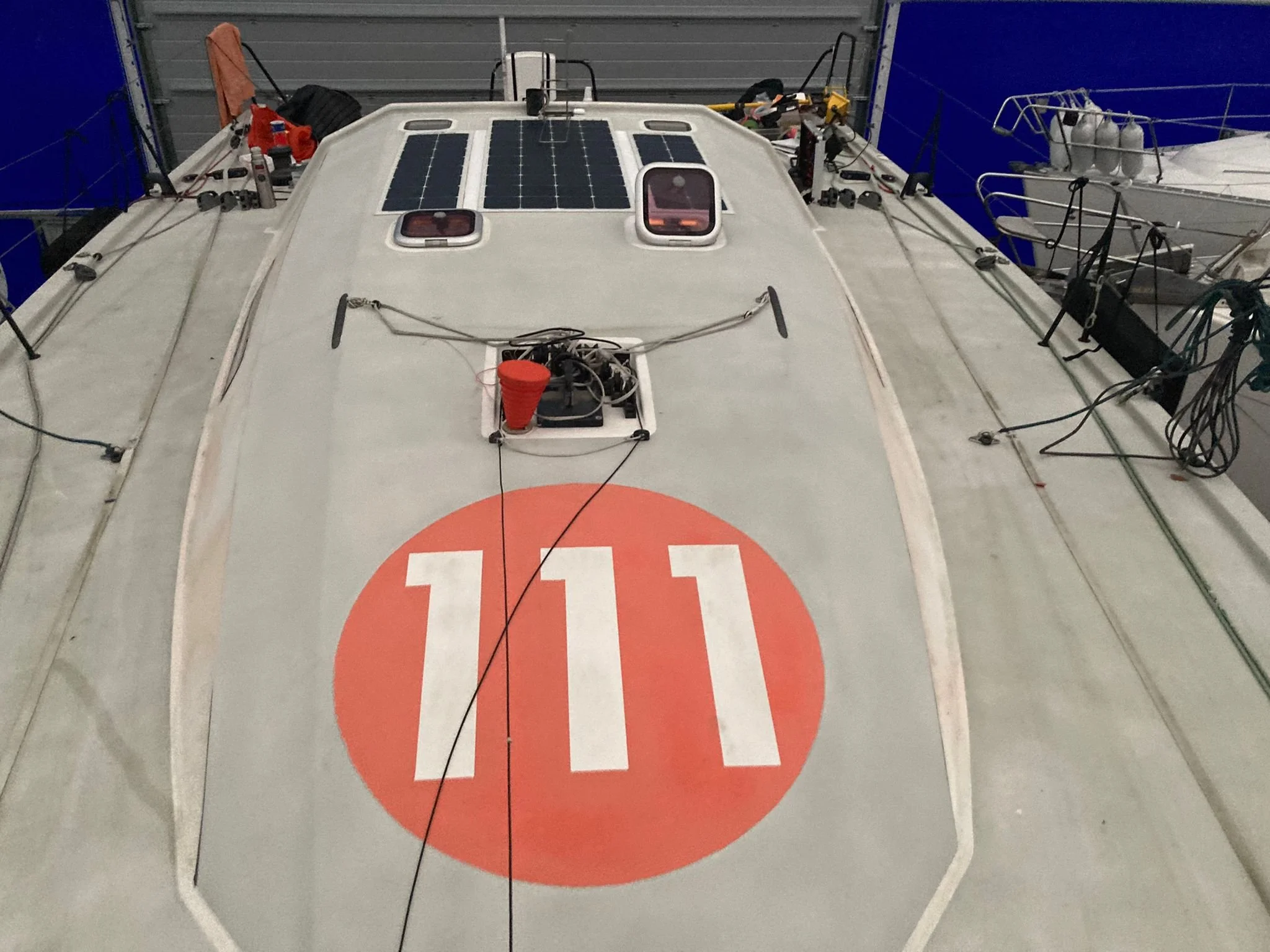 Front of a boat with solar panels on the roof, anchor line, and emergency equipment, in a storage or garage area.