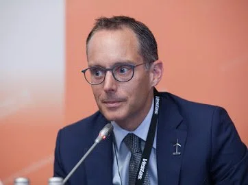 Man with glasses and a conference badge speaking into a microphone at a meeting