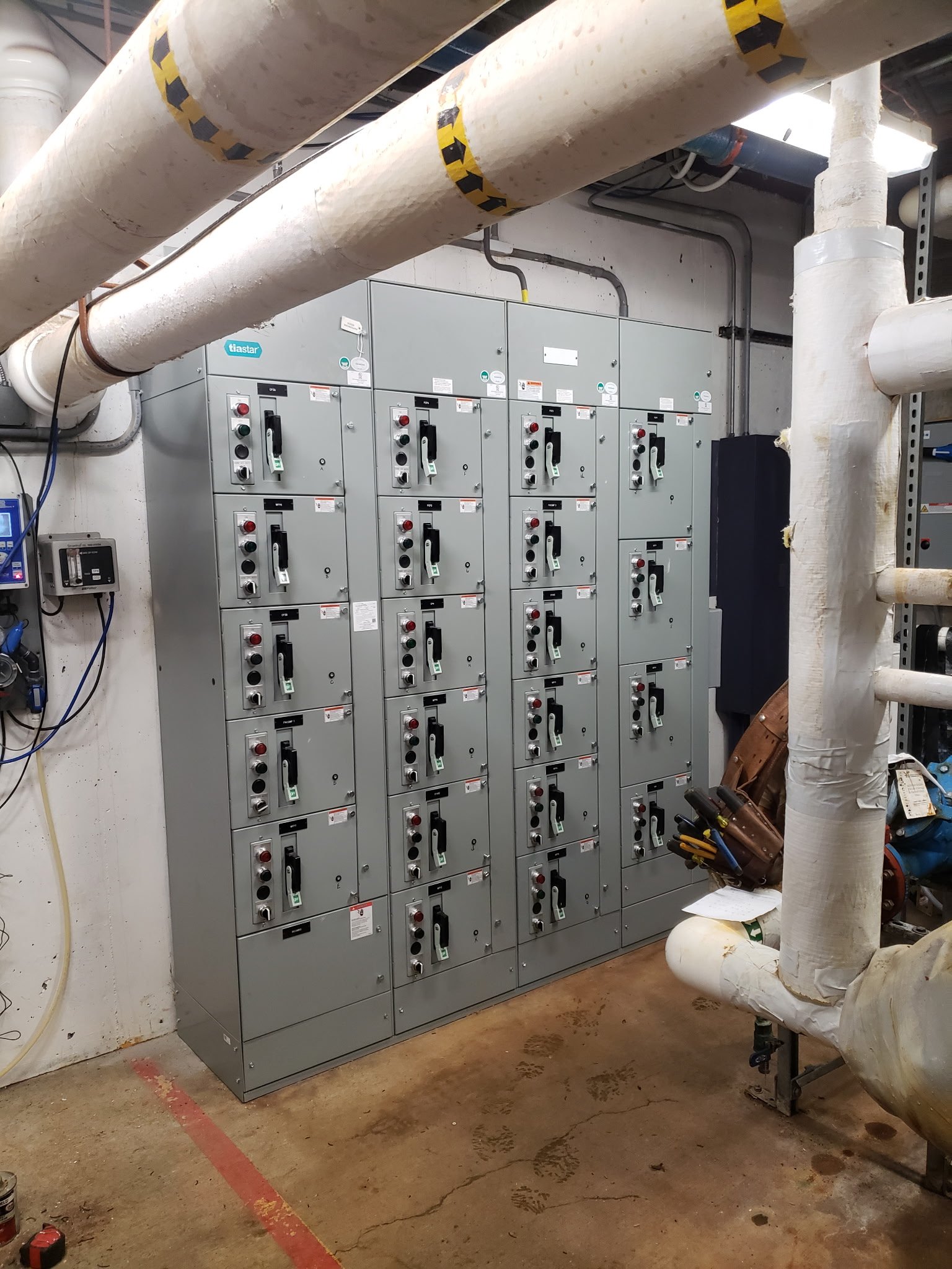 Electrical panel with circuit breakers and large white pipes in a utility room.