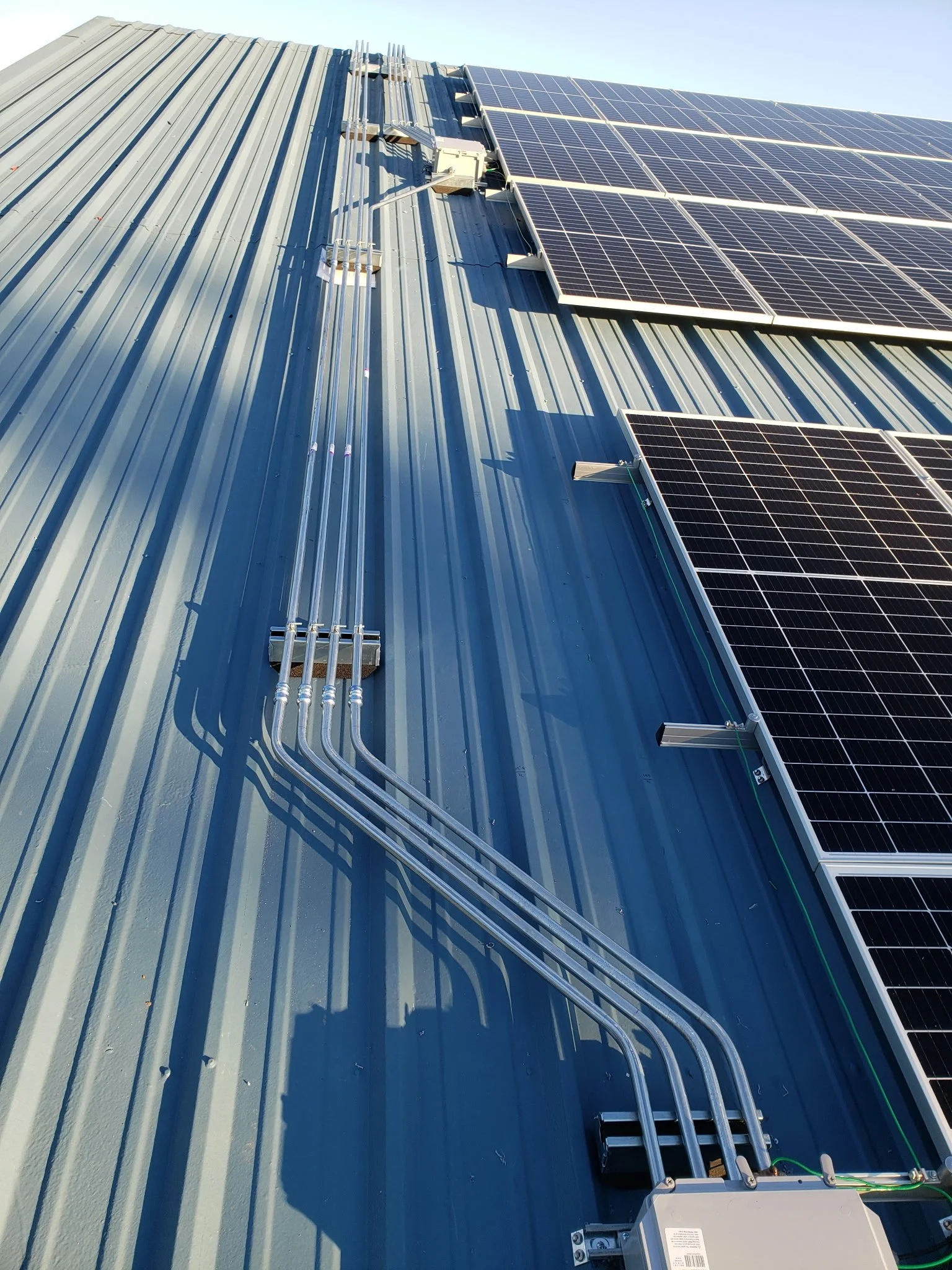 Solar panels installed on a blue metal roof with electrical wiring and conduit.