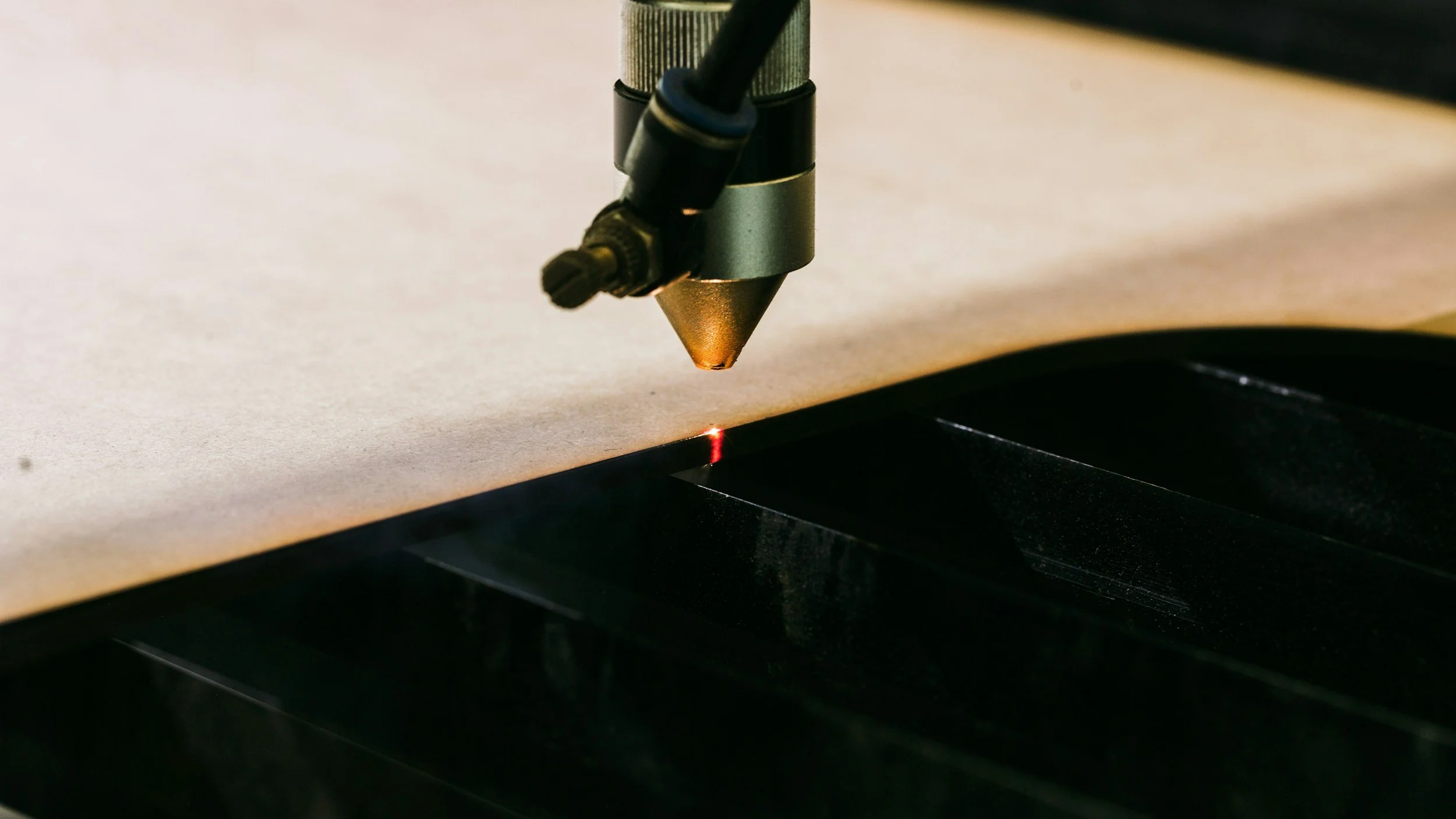 A laser cutter head emits a red laser beam onto a sheet of material, with a black tray or platform underneath to catch debris.