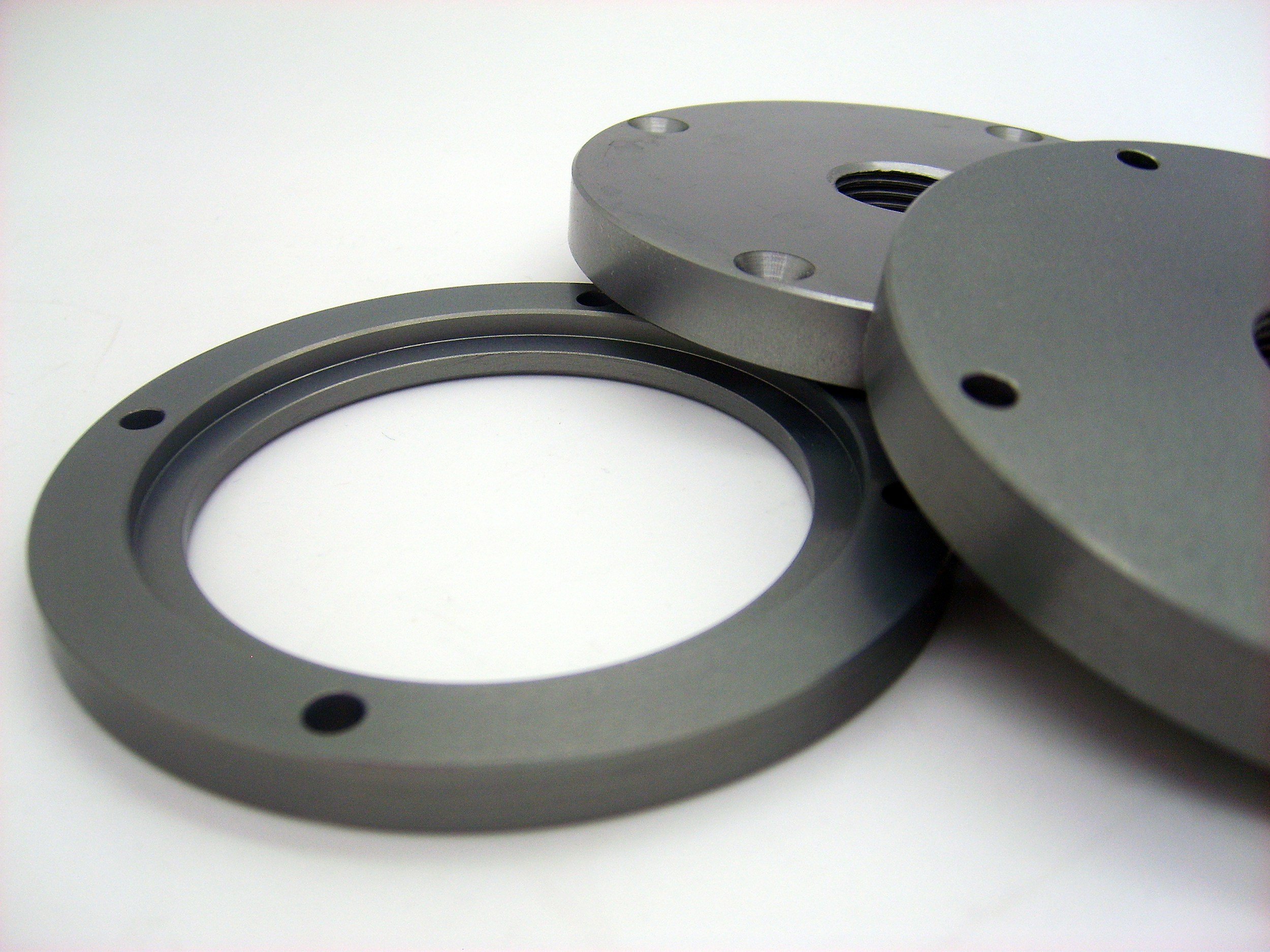 Close-up of metallic mechanical components, including a circular ring and two larger circular pieces, placed on a white surface.