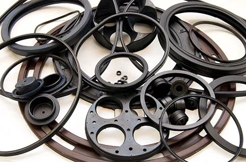 Assortment of black rubber and plastic O-rings and gaskets of various sizes scattered on a surface.
