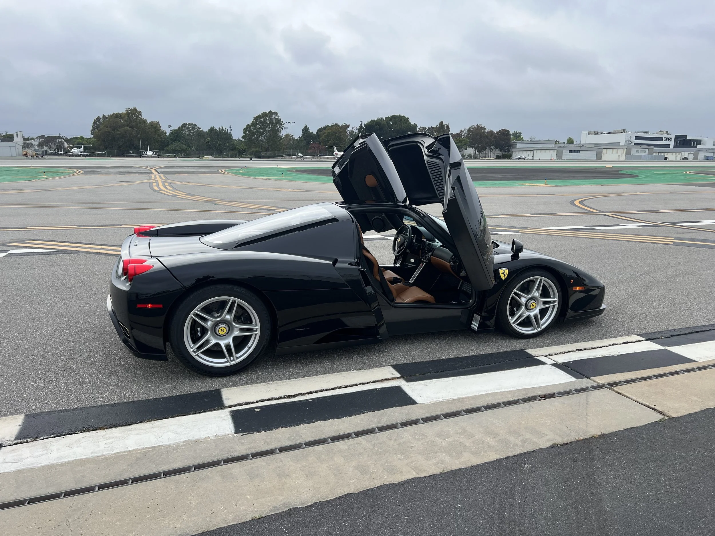 A black Ferrari sports car with gullwing doors open, parked on an airport tarmac.