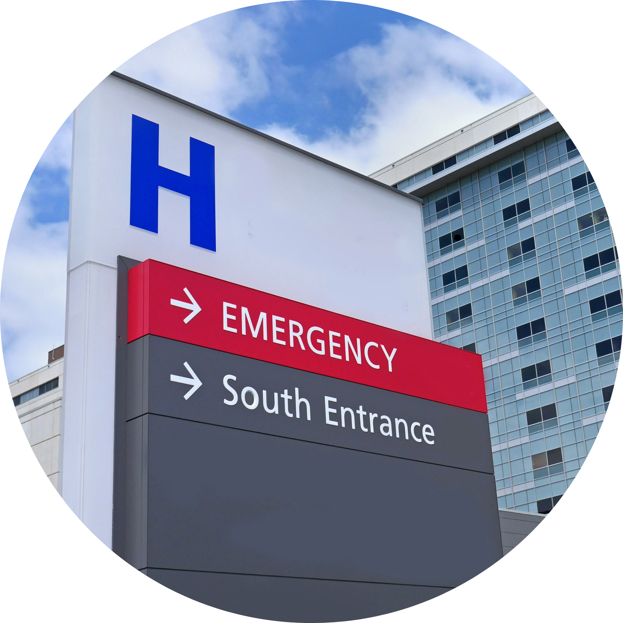 Hospital building with a large blue 'H' sign and a red and black directional sign indicating emergency and south entrance, set against a partly cloudy sky.