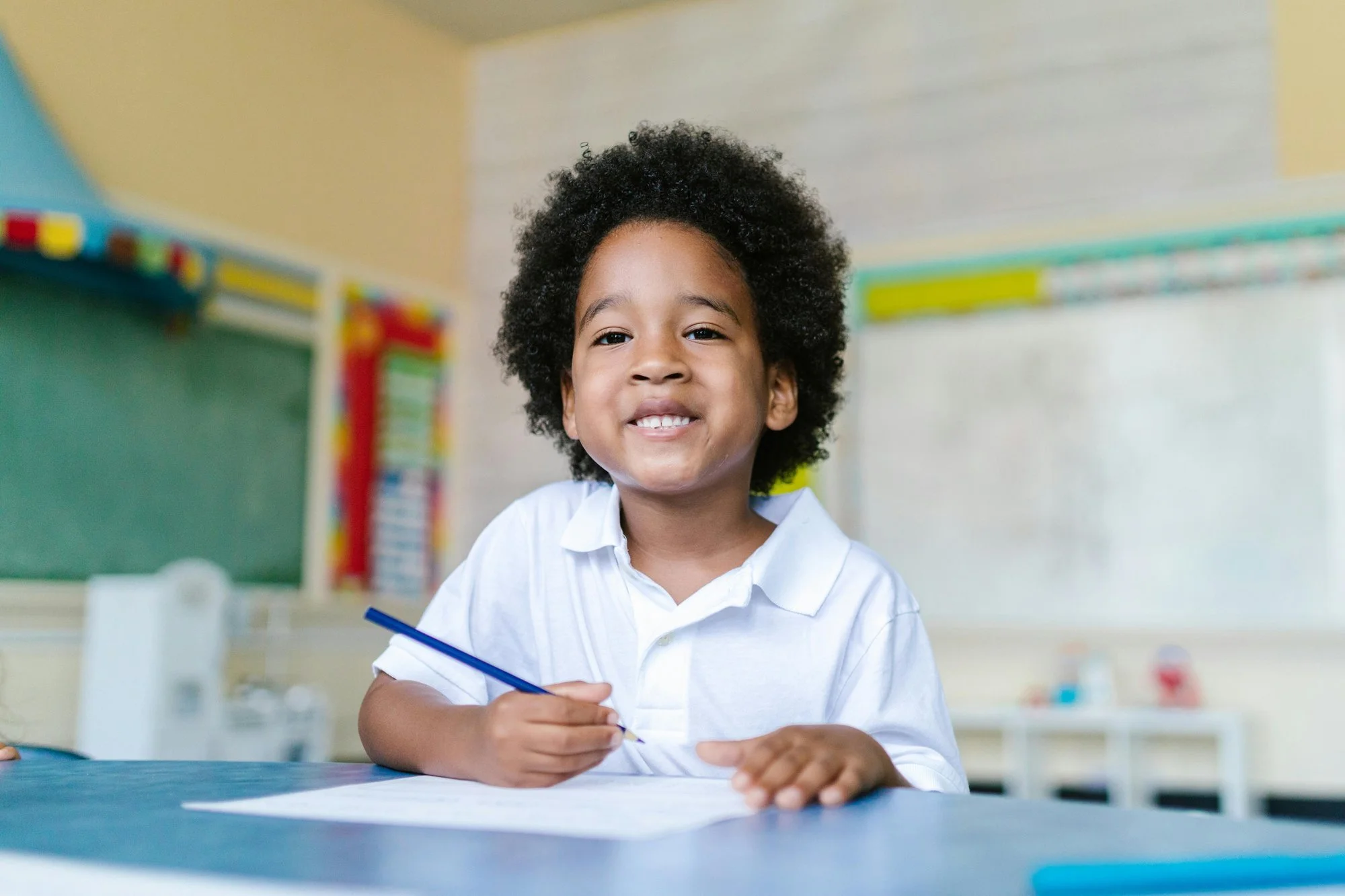 Elementary student smiling while writing at a classroom desk.