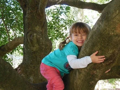 Child smiling while hugging a tree during an outdoor learning activity.