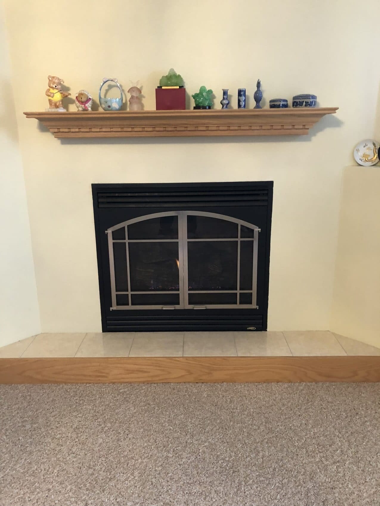 Fireplace with a black metal screen and a wooden mantel decorated with small figurines, glass objects, and decorative items on top.