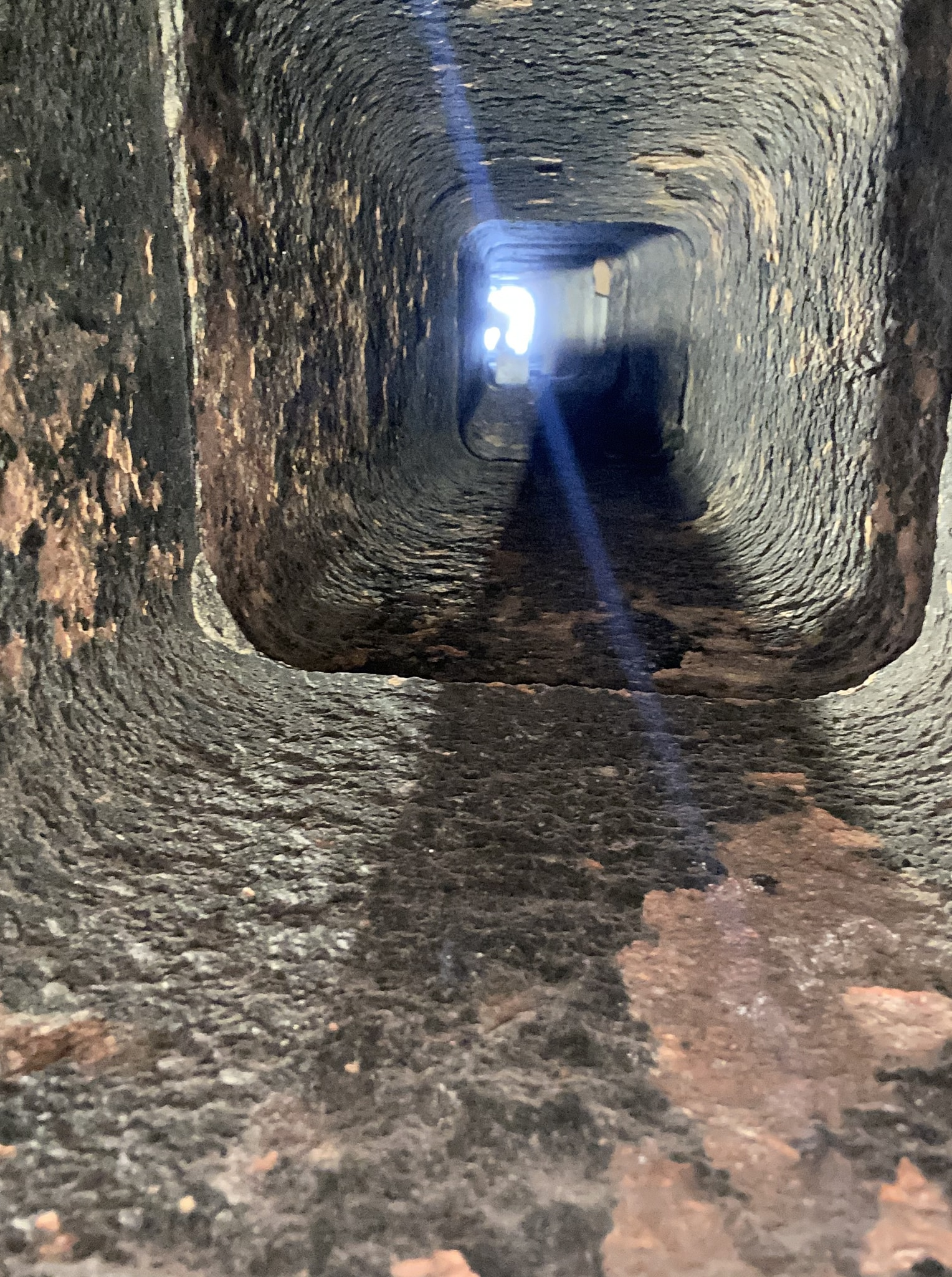 Looking into a sewer pipe, showing the interior with textured walls and natural light coming from a distant opening.
