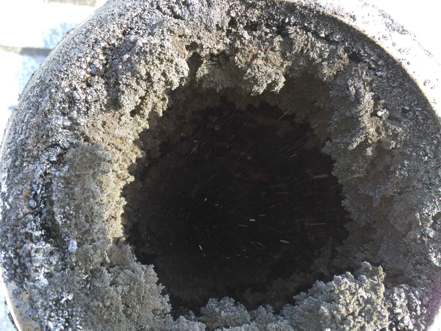 Close-up of a dark, hollow pipe with frost and ice crystals forming on the inner and outer edges.