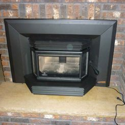 A black fireplace insert with glass door installed in front of a brick wall, with a power cord plugged in.