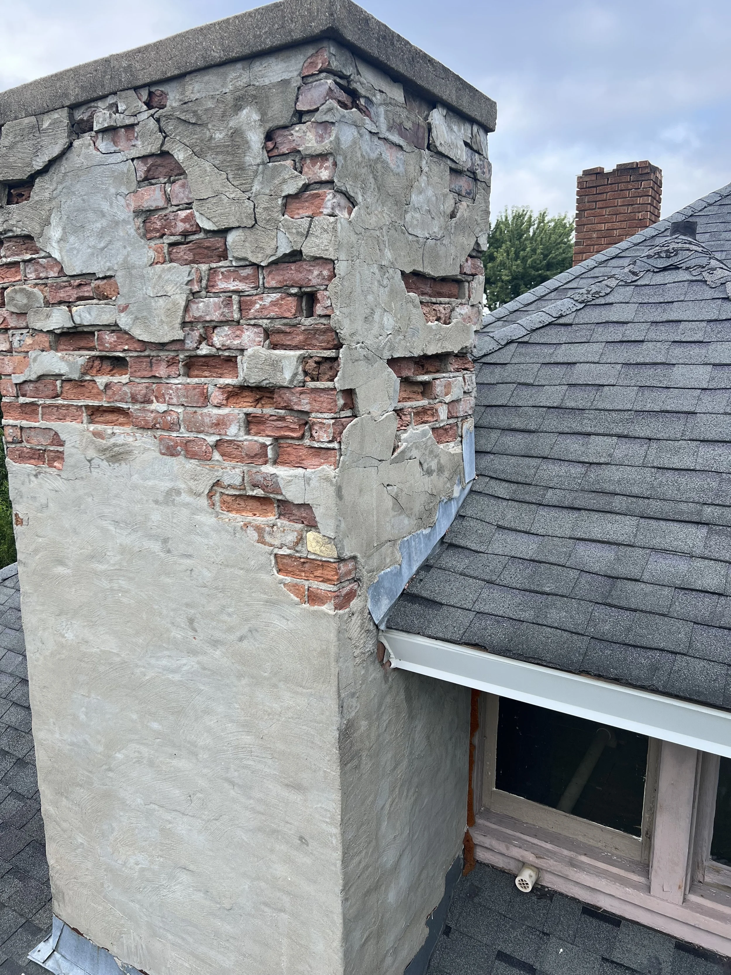 A chimney under construction showing bricks and concrete with a roof in the background.
