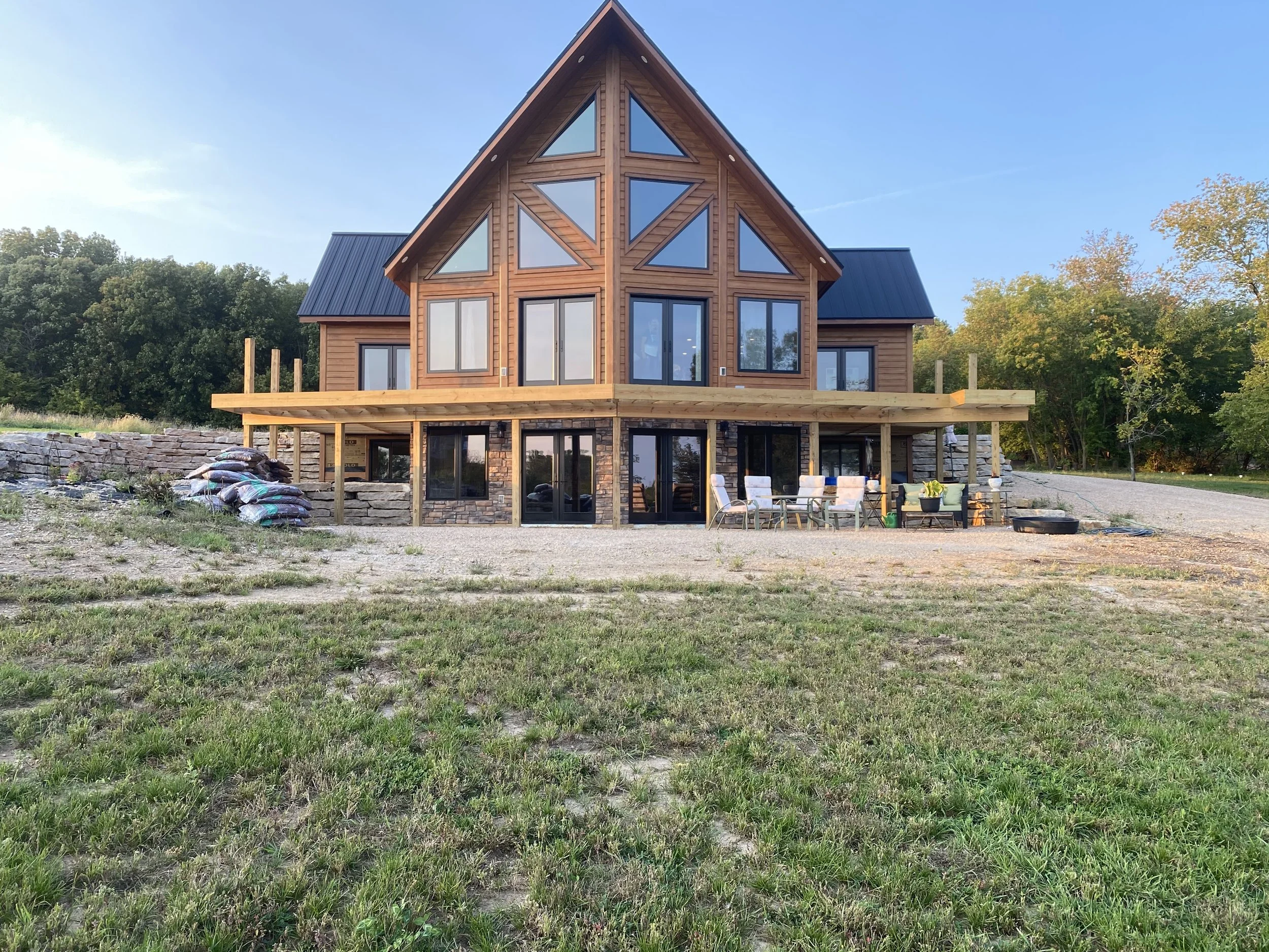 A modern A-frame house with large triangular windows and a dark metal roof, situated on a grassy lot with trees in the background.