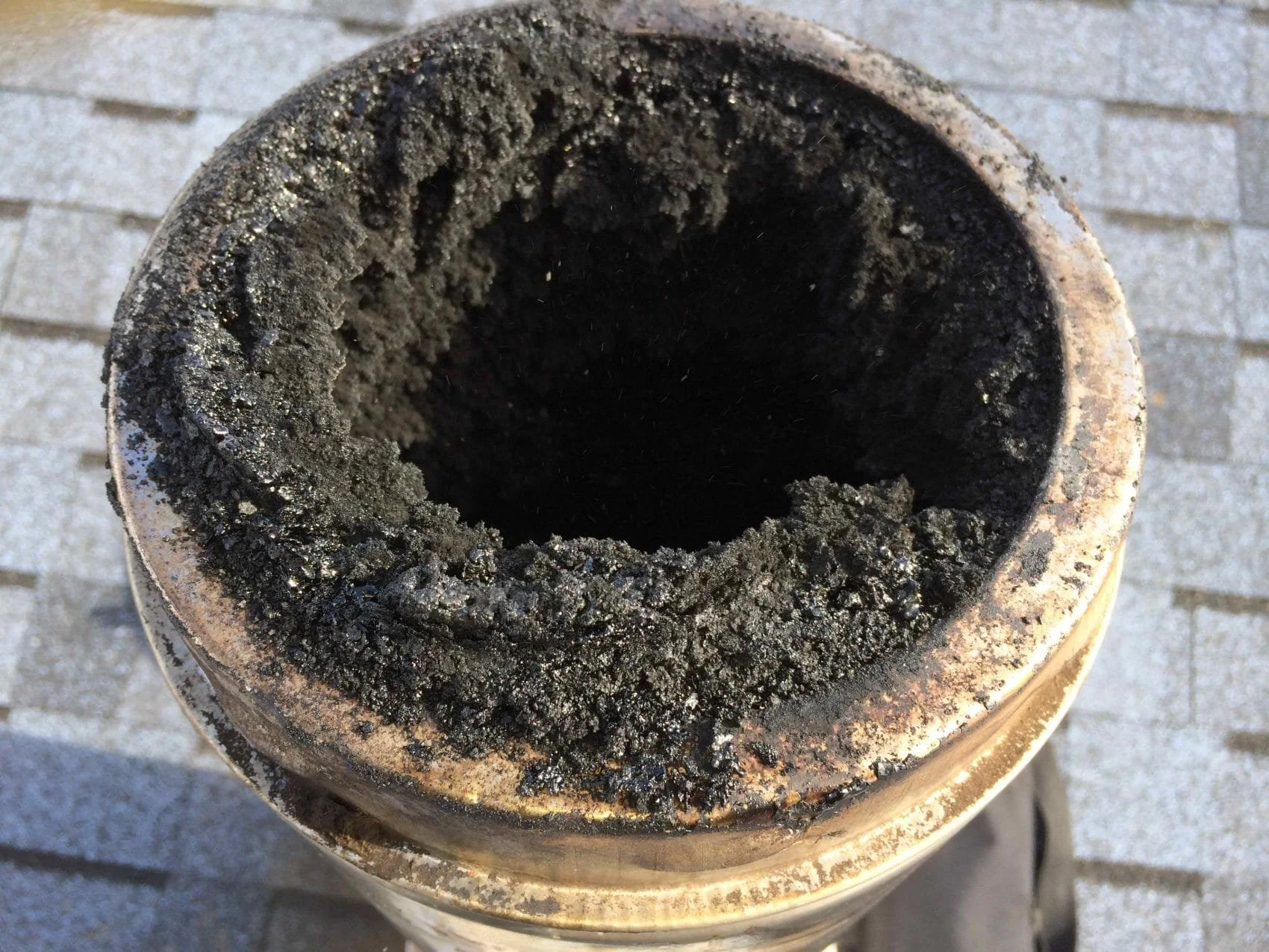 Close-up of a pipe or tube opening clogged with black soot or ash, with a brick wall visible in the background.