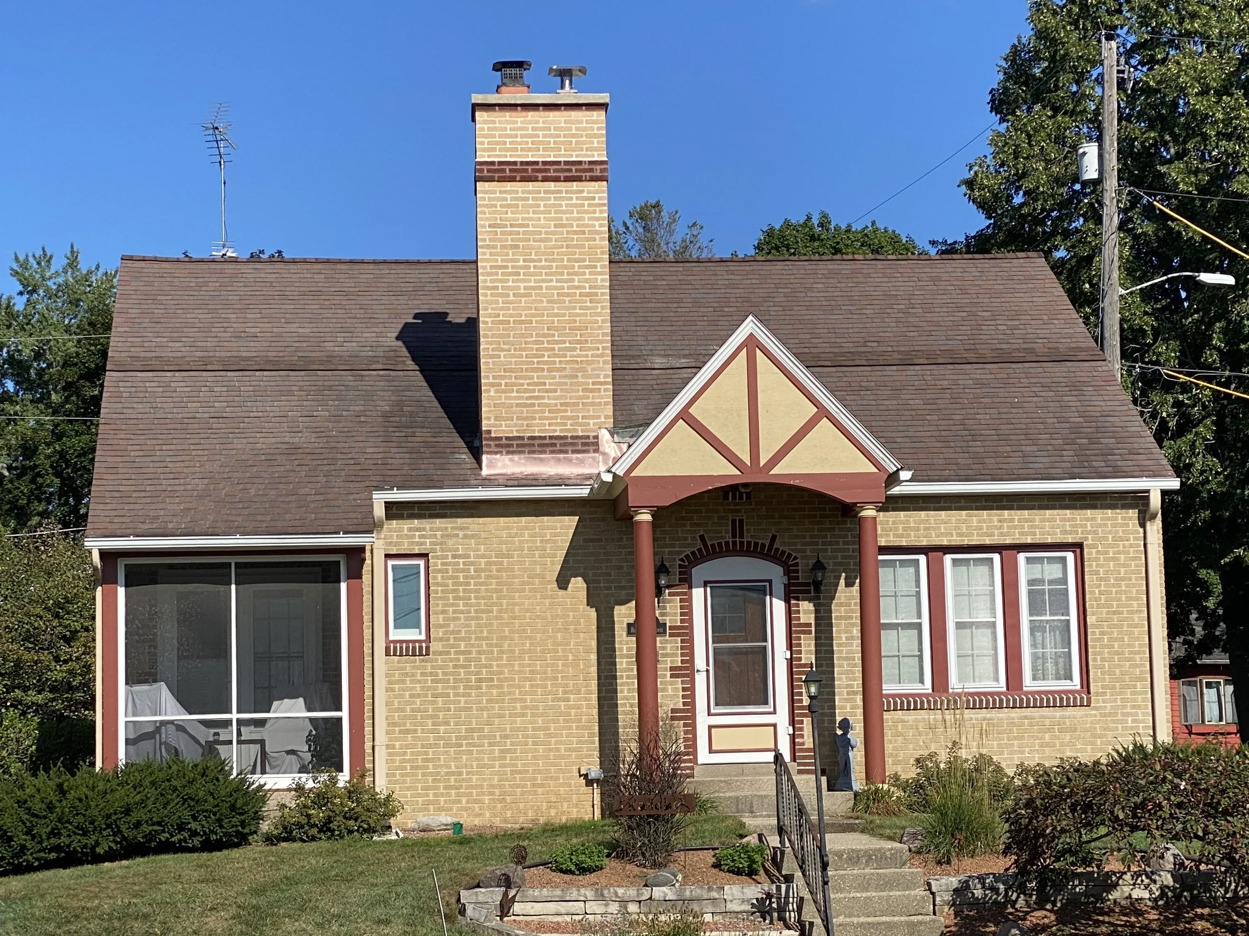 Front view of a two-story house with brick exterior, large windows, a prominent brick chimney, and a small front garden with stairs leading to the front door.