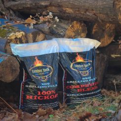 Two bags of Timber Jack premium charcoal briquettes placed on the ground near rocks and wood logs.