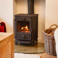 Electric fireplace heater with a visible flame effect, black in color, placed on hardwood floor near a wicker basket and red object.
