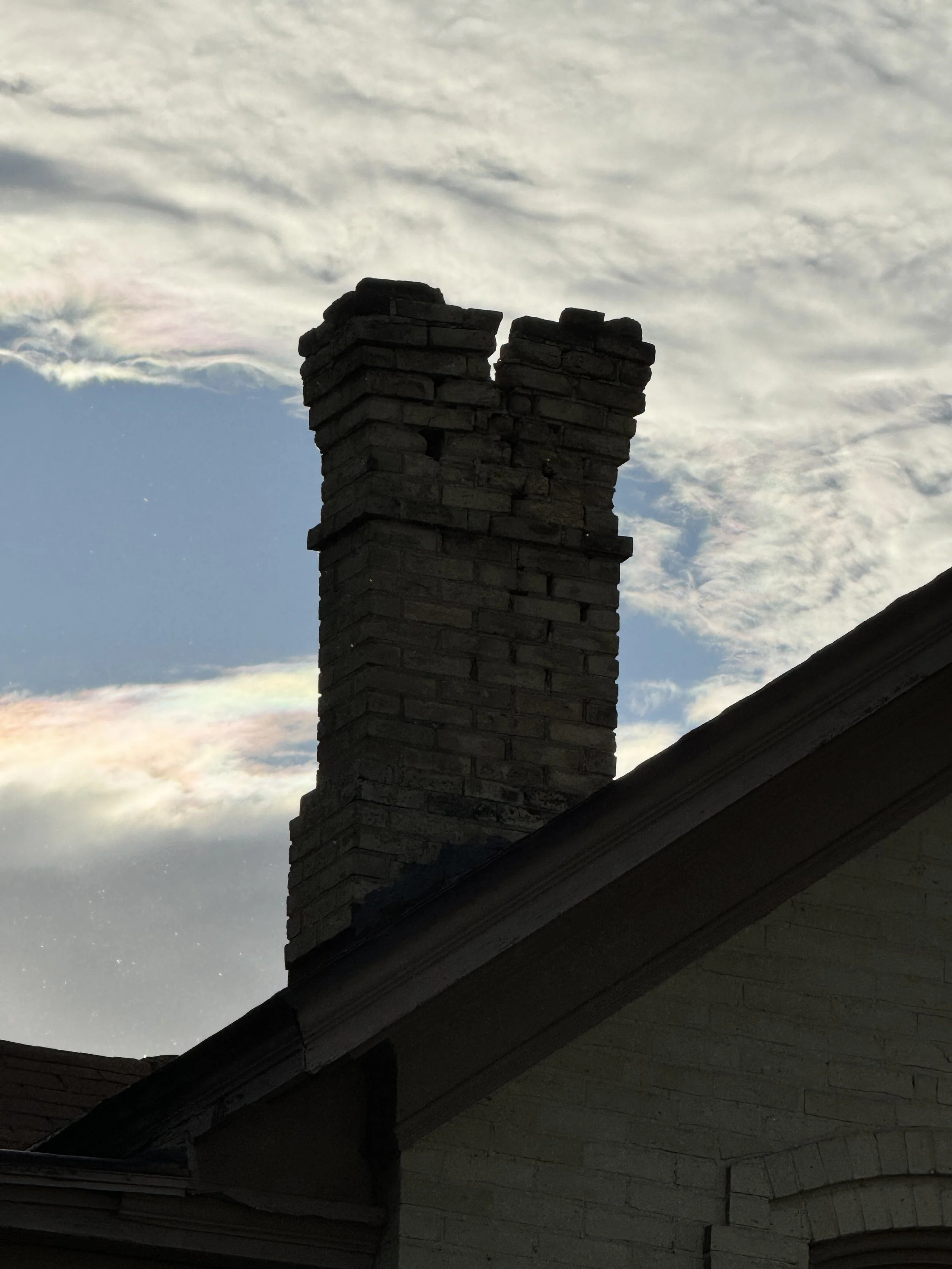 A brick chimney on a house with a cloudy sky in the background.