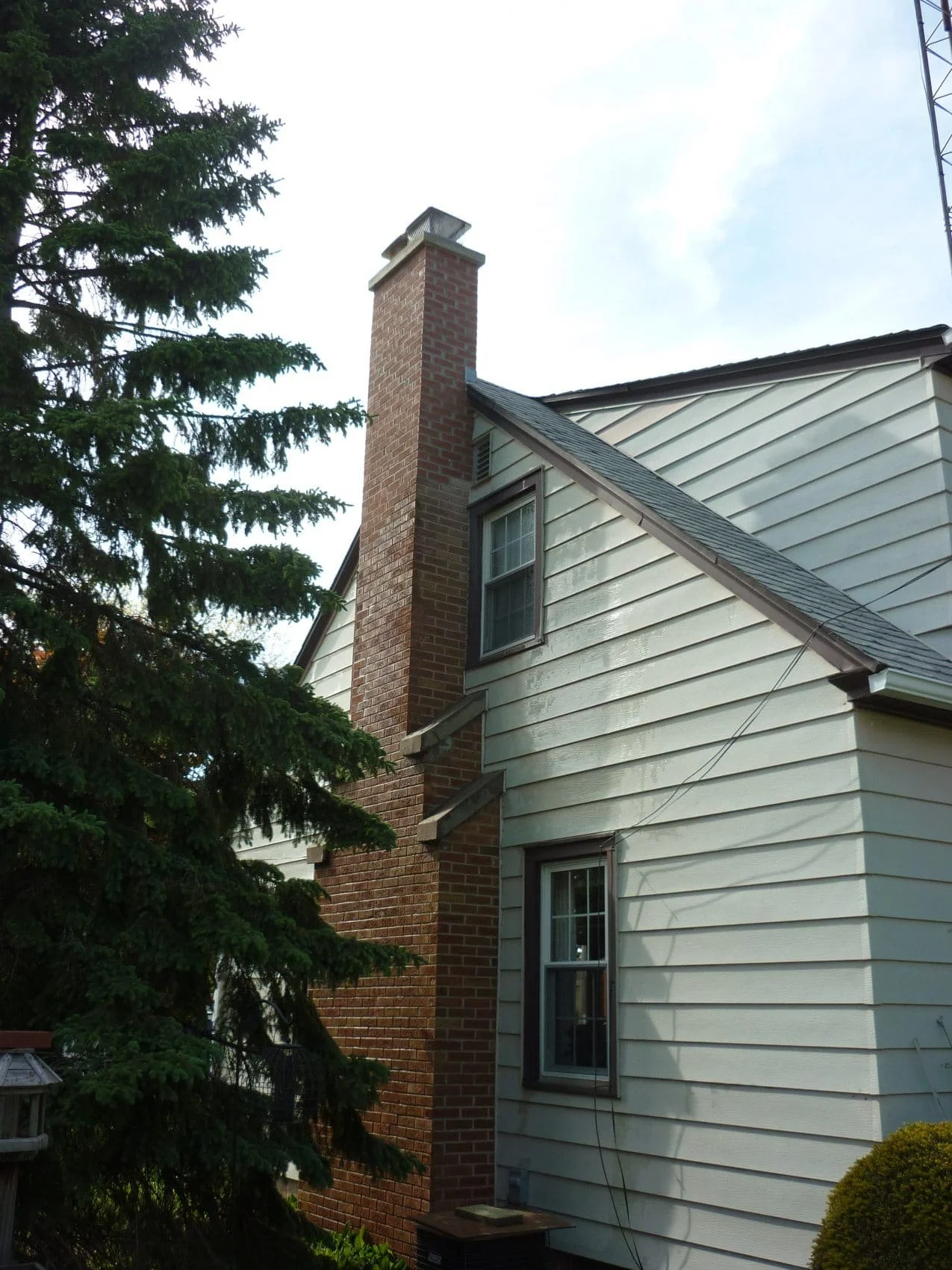 A house with white siding and a brick chimney, with a tree on the left side and a partly cloudy sky in the background.
