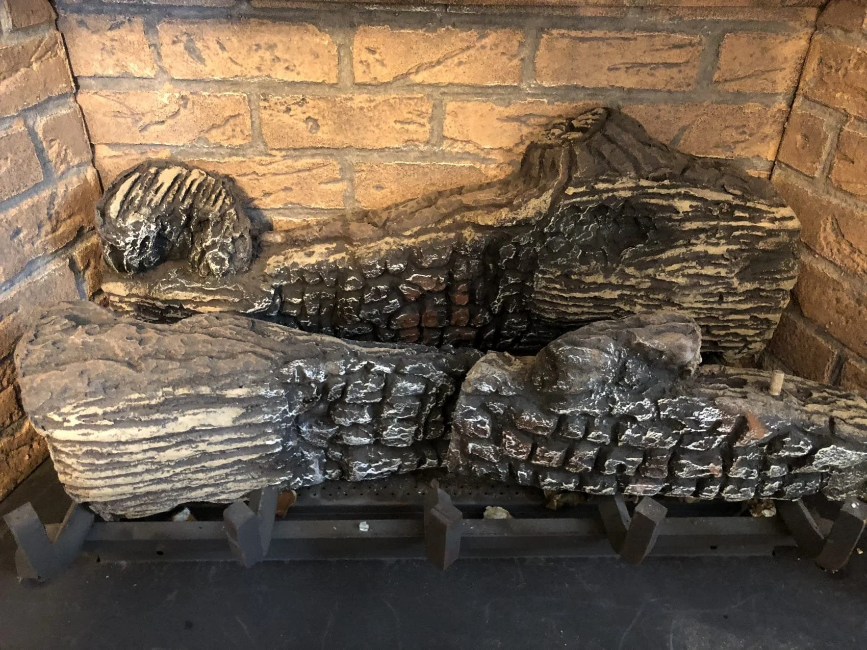 A collection of weathered, dark-colored logs with distinct rings and textured surfaces, placed against a brick wall background.