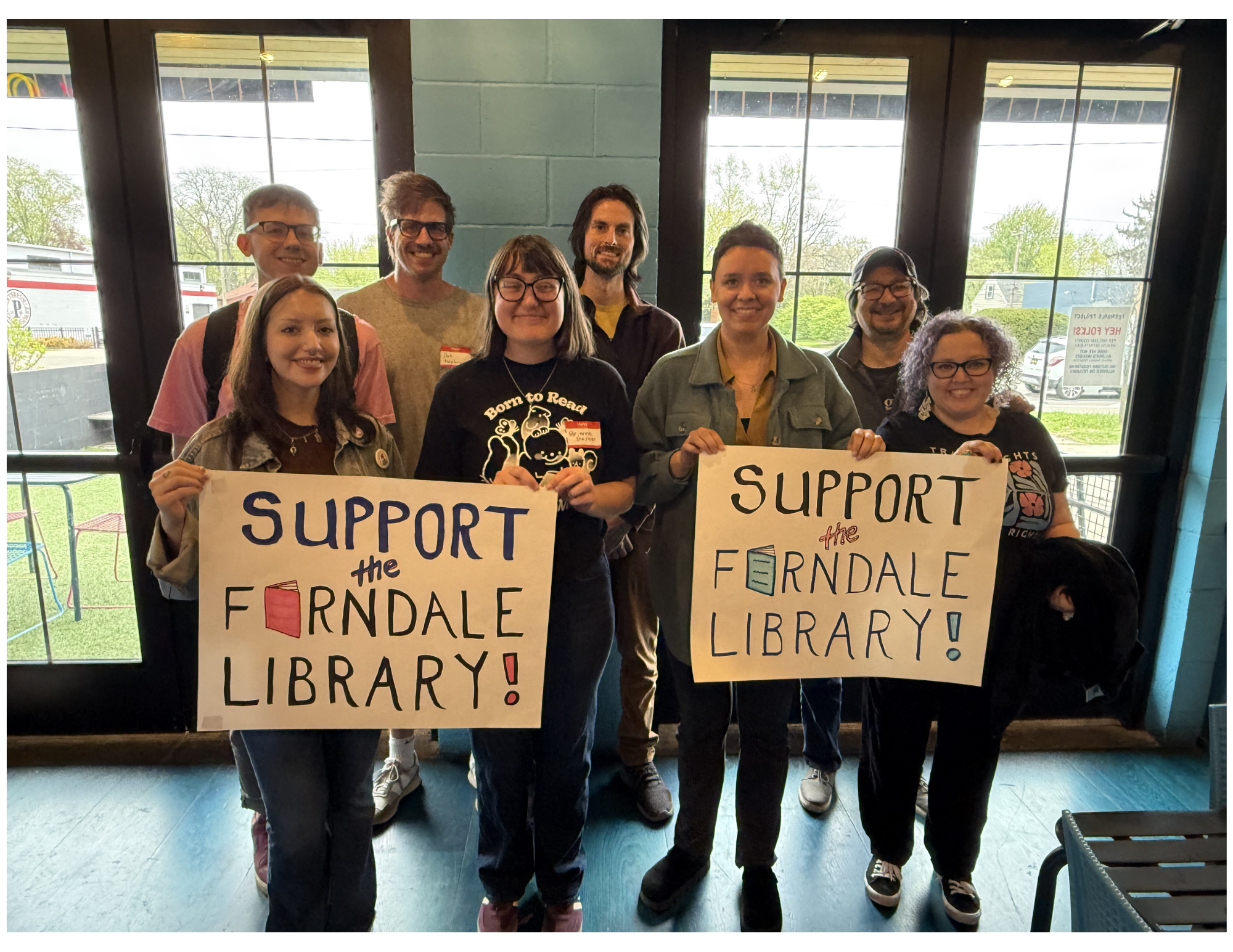 Ferndale residents and YES Ferndale Library volunteers happily stand together displaying hopeful signs of support.
