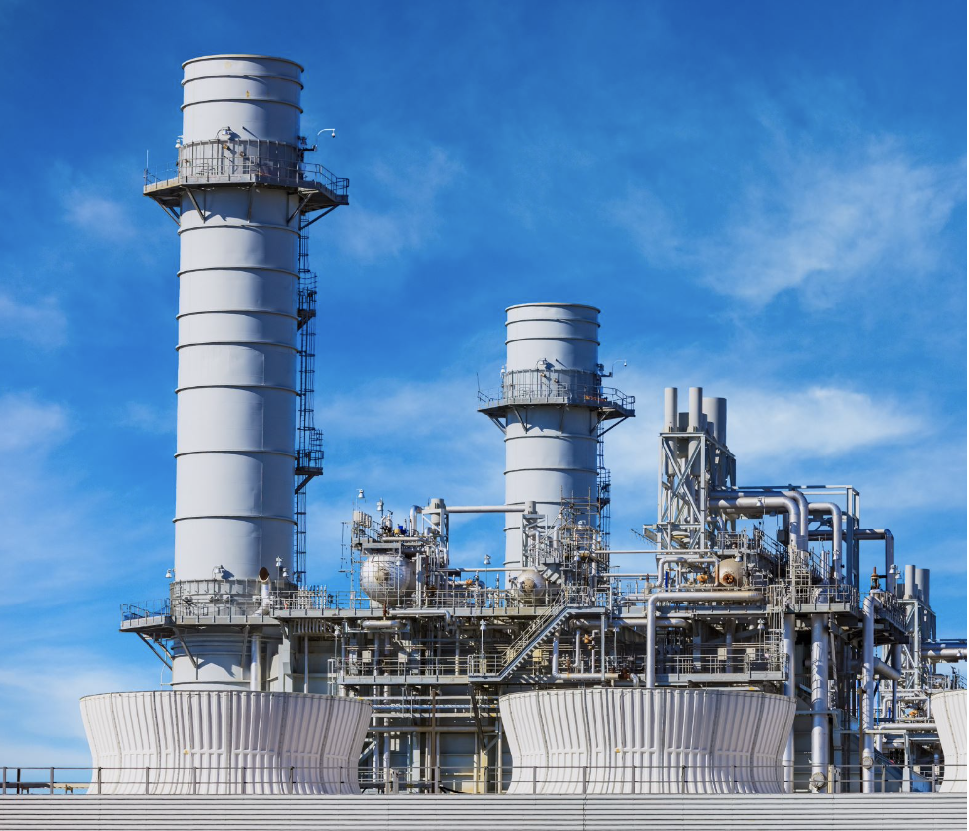 Industrial refinery with tall white smokestacks and complex piping against a blue sky.