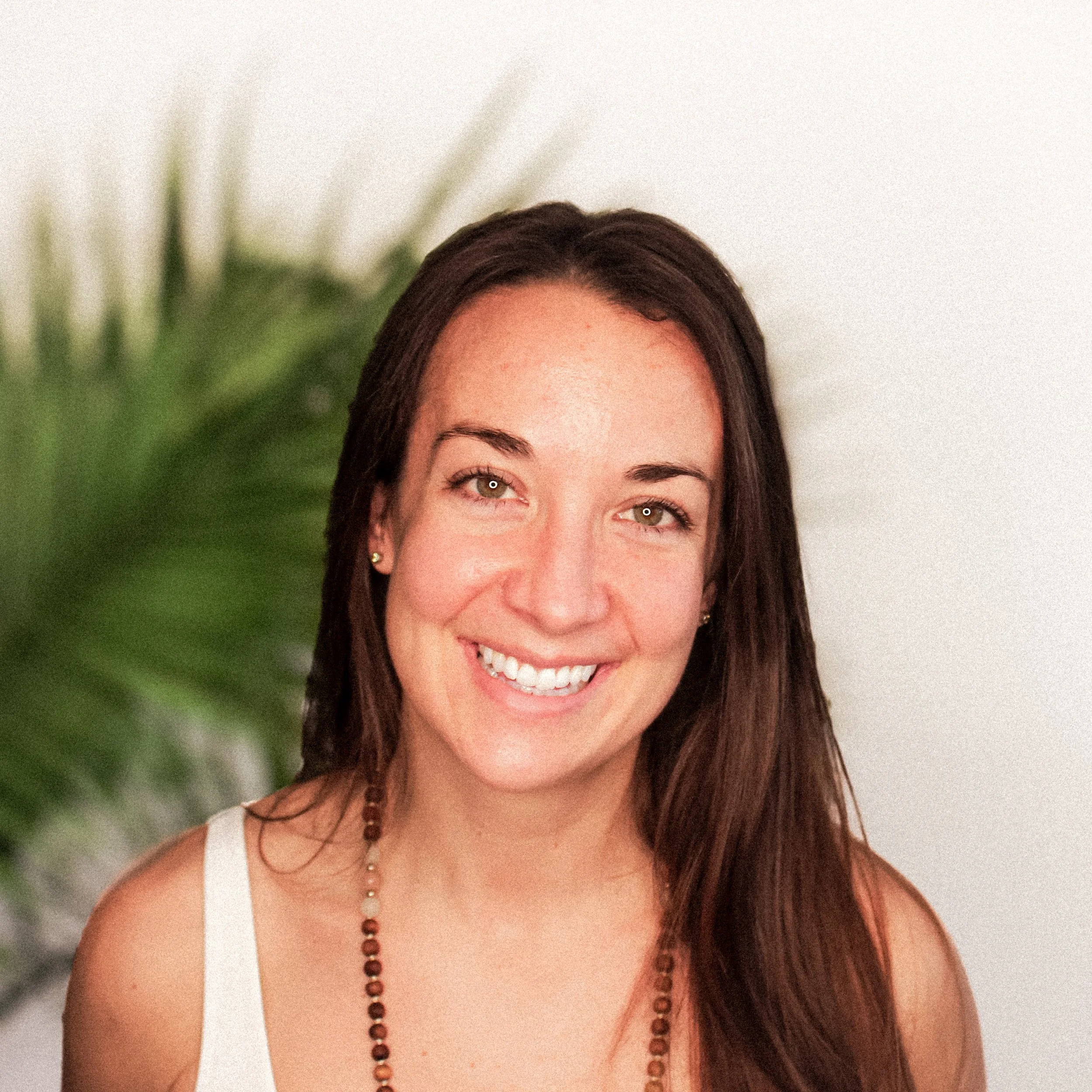 MYA Director of Marketing and owner of Bent9 Hot Yoga, Hannah Skiba smiling with a blurred green plant in the background
