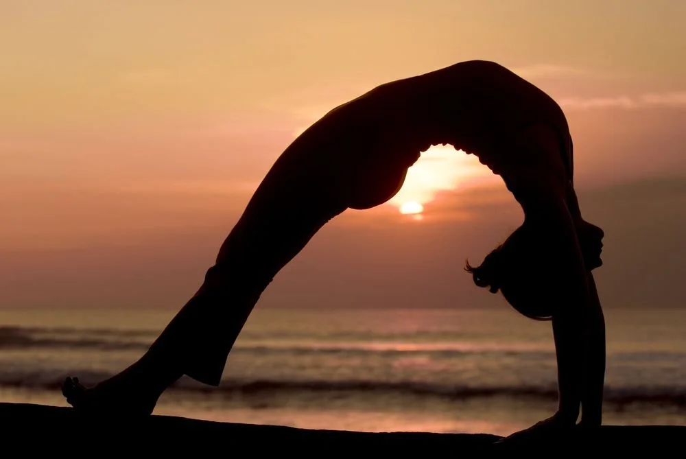 Silhouette of a woman performing a yoga pose on the beach at sunset.