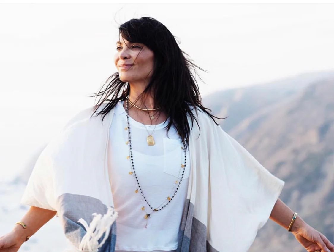 Amanda Giacomini with open arms in front of breezy mountain coast