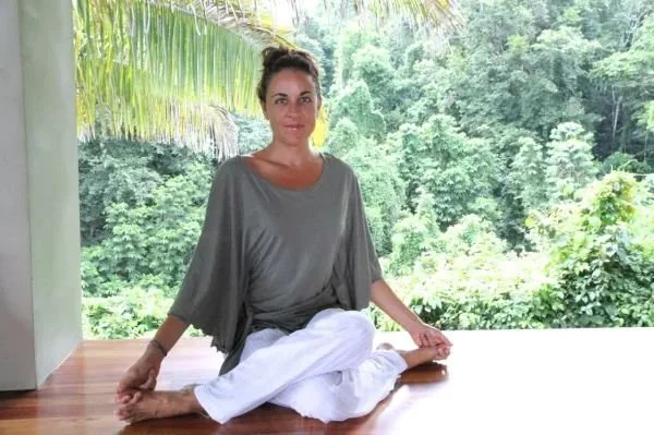 Indira Kate Kalmbach, M.A., LPC, in seated yoga position with forrest behind