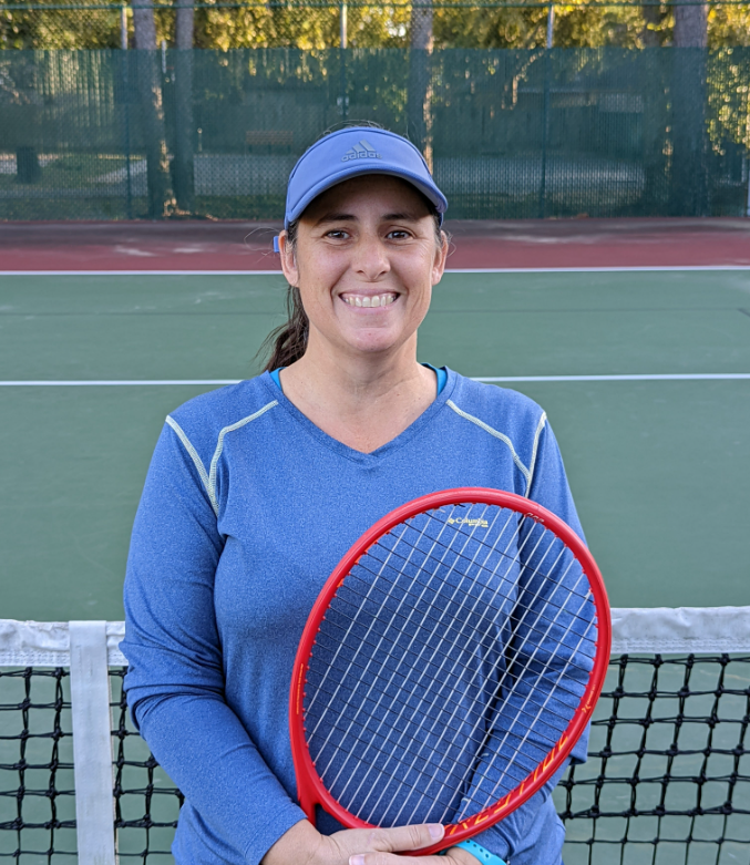 A woman in a blue athletic shirt and hat holding a red tennis racket on a tennis court.