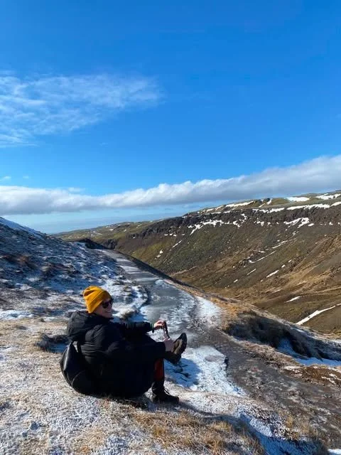 Person sitting on a snowy hillside overlooking the Icelandic landscape.