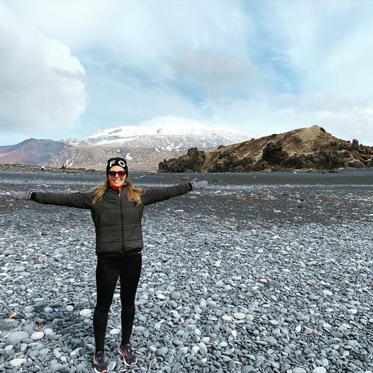 Woman standing on an Icelandic beach with volcanic mountains and snow in the background.