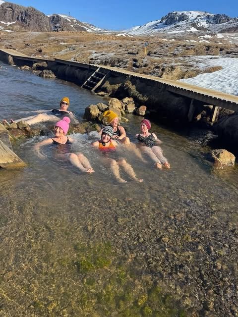 People swimming in a shallow Icelandic thermal stream surrounded by mountains and snow.